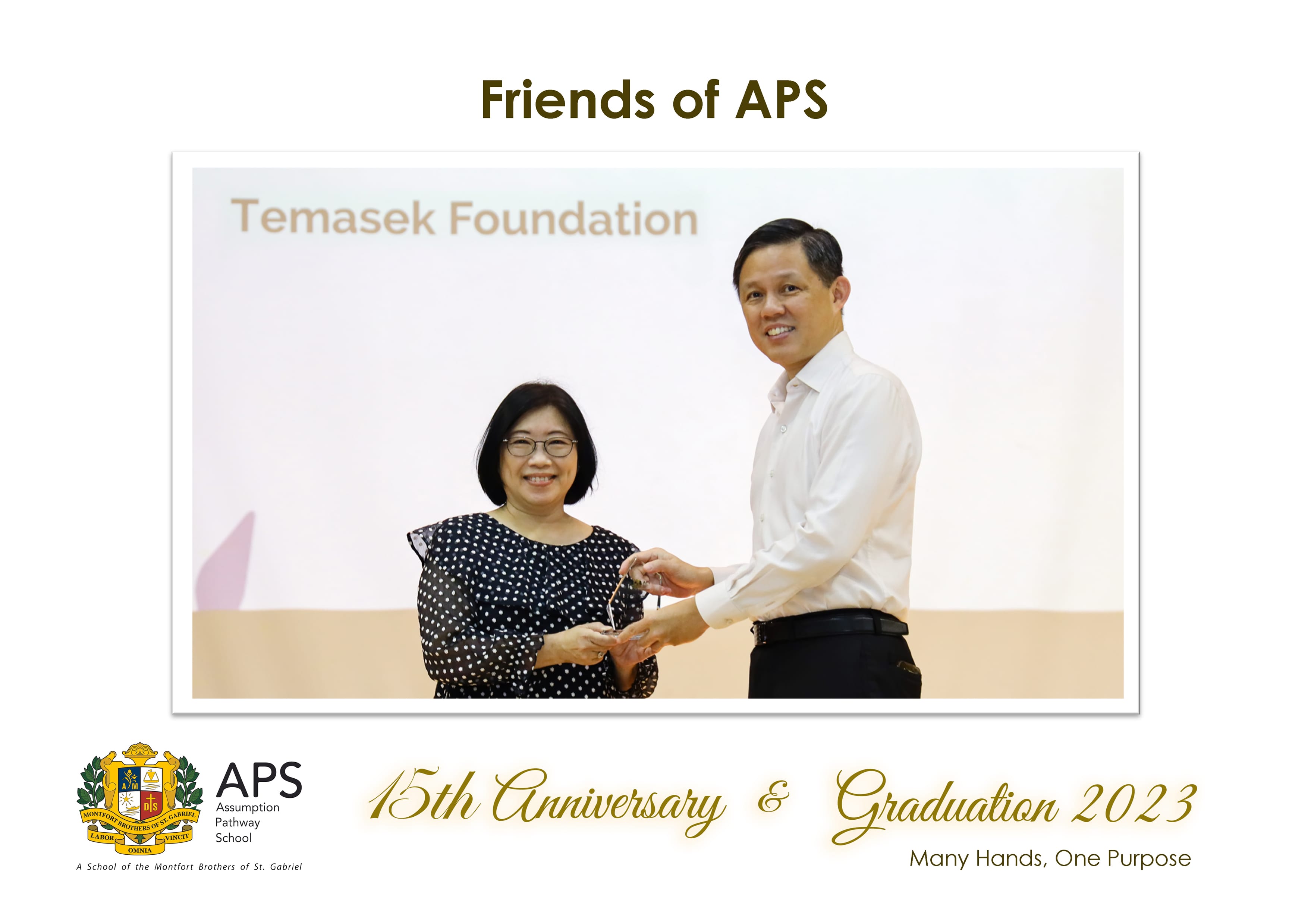 Two people smiling and exchanging a small award in front of a Temasek Foundation backdrop at APS Graduation 2023.